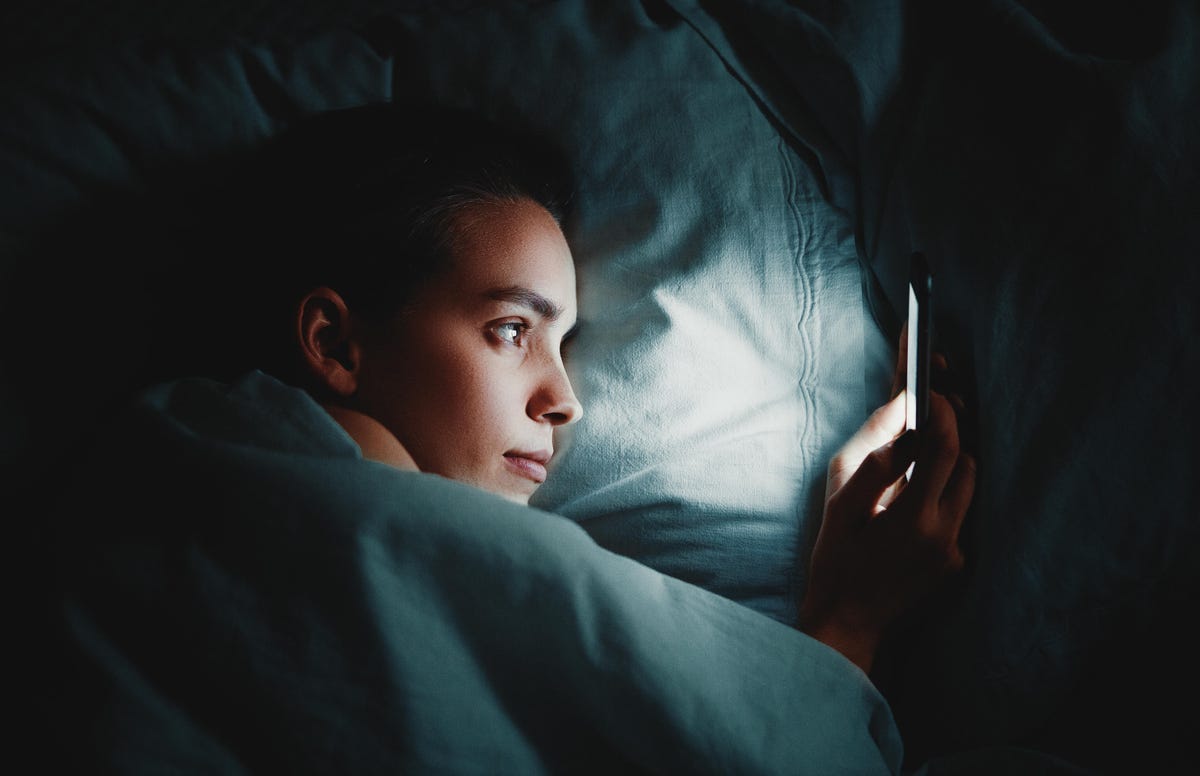 Closeup of a woman using a phone while lying in bed in a dark room