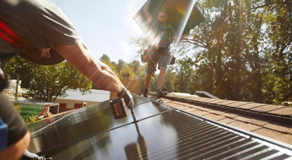Solar installers put panels on a roof.