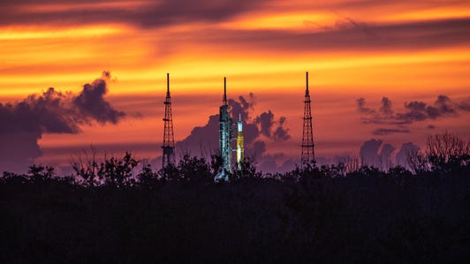 Sunrise glows in deep purples, red and yellows behind the Artemis I moon rocket in Florida.