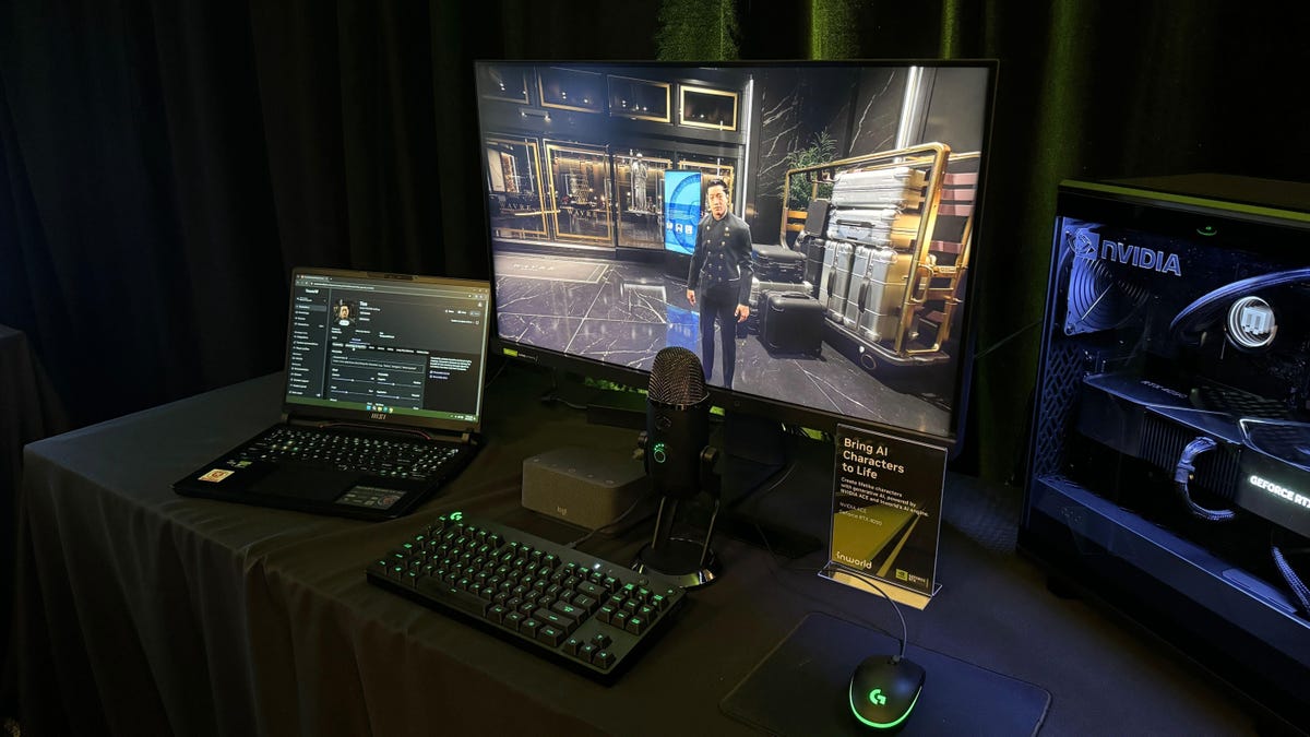 A computer desktop, keyboard and monitor showing a first-person game sit on a black tablecloth-covered table. A laptop with game data also sits on the table.