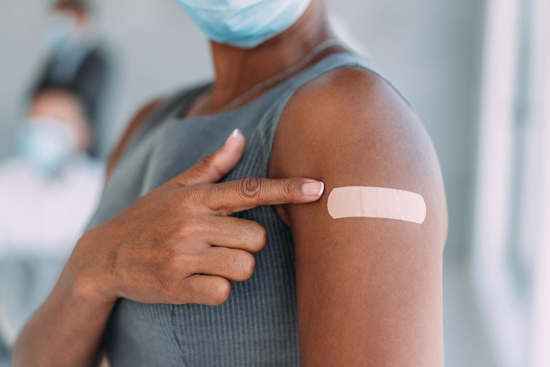 A woman points to a bandage on her arm after receiving a shot.