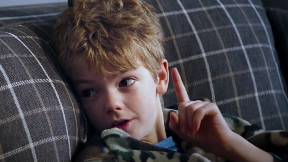 Midshot of a young boy sitting on a couch holding up one finger