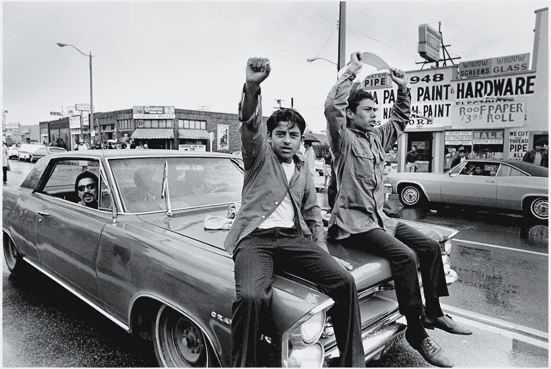 Two young men from Chicano are riding on the hood of a car
