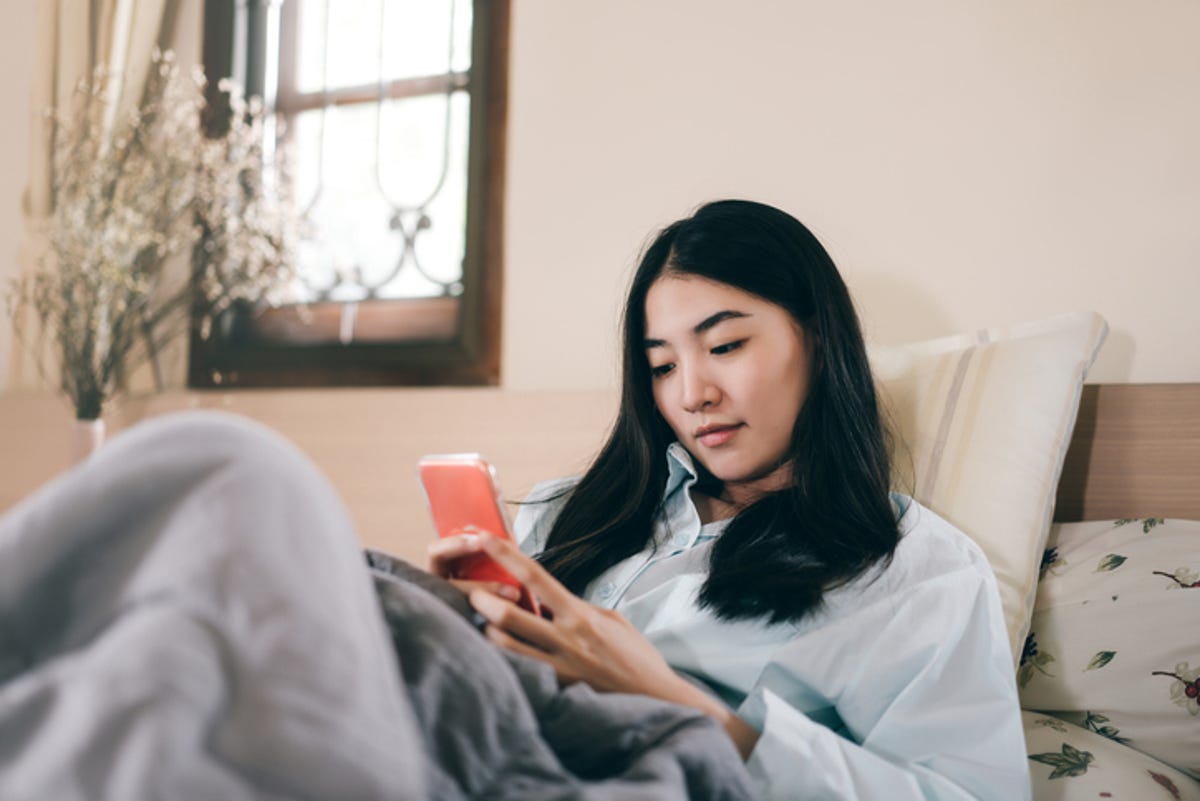 Young woman lounging in bed, scrolling through her phone.