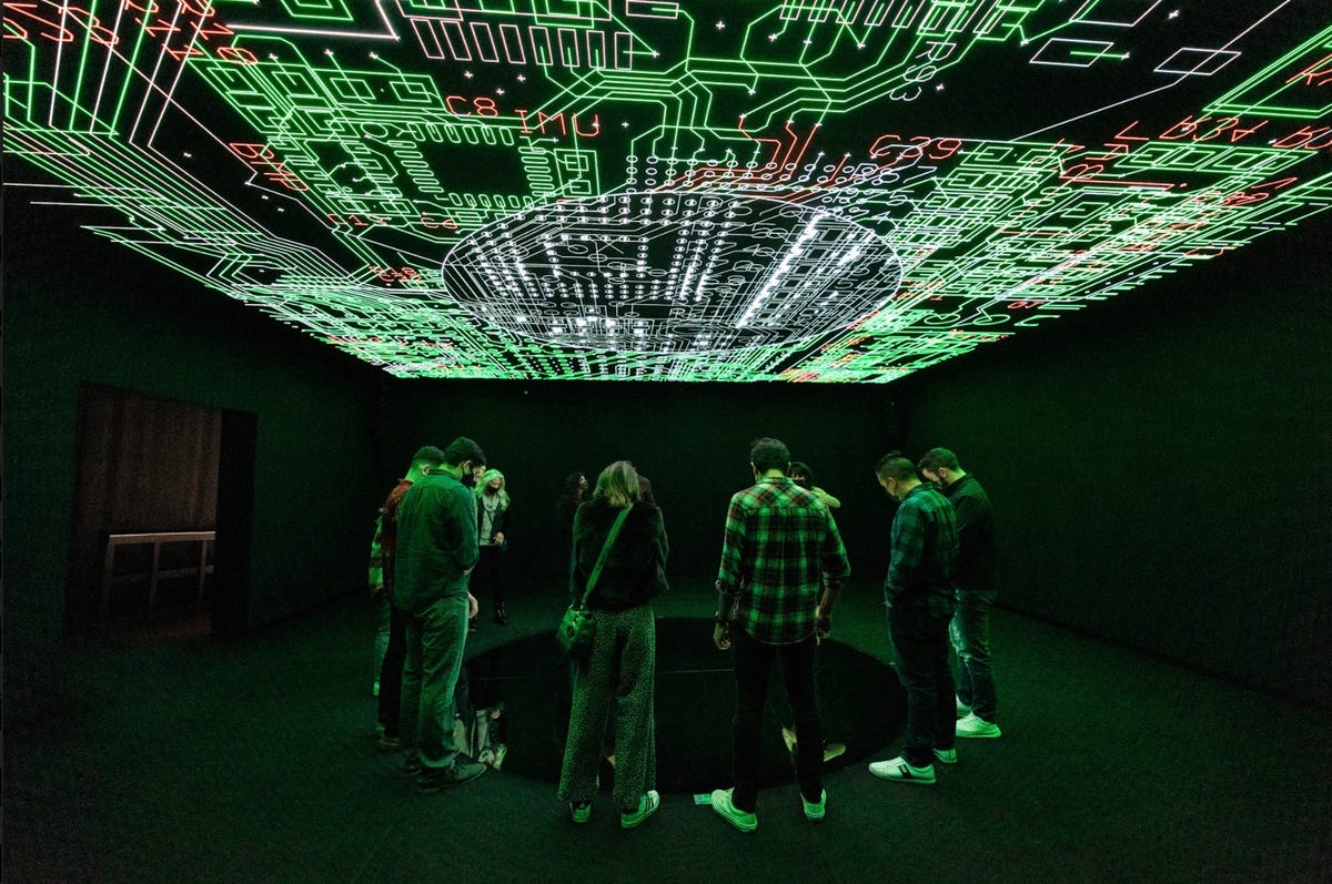 A group of people stands underneath video art installation playing on the ceiling