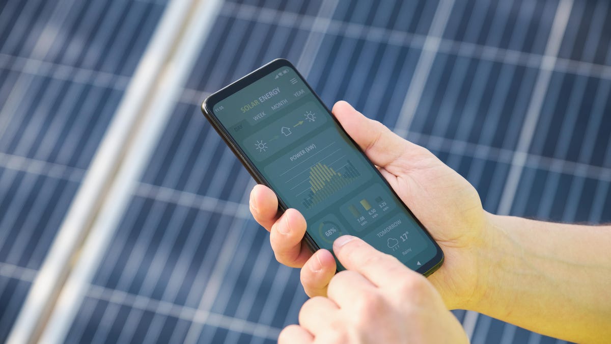 Close-up on a person checking the activity of solar panels on a rooftop using a cell phone app