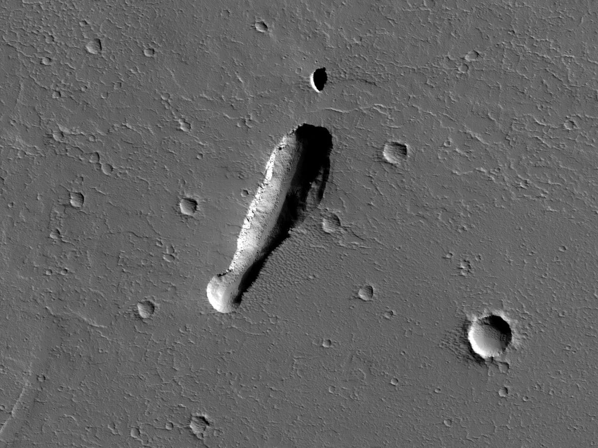 Black-and-white overhead view of Mars landscape with a heavily shadowed elongated pit. Image is oriented upside-down.