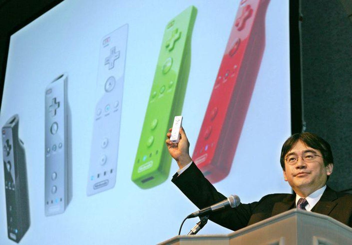 Wii remote held up by Satoru Iwata on stage, in front of an image of Wii remotes.