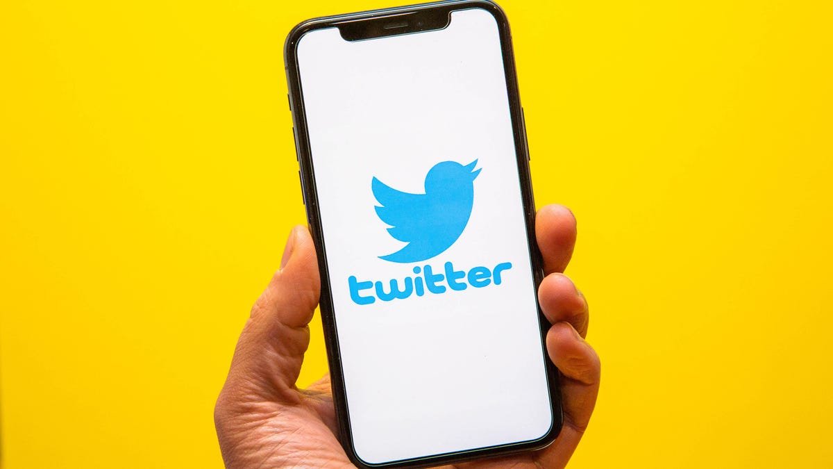 Photo illustration of hand holding a smartphone with Twitter's logo on the screen