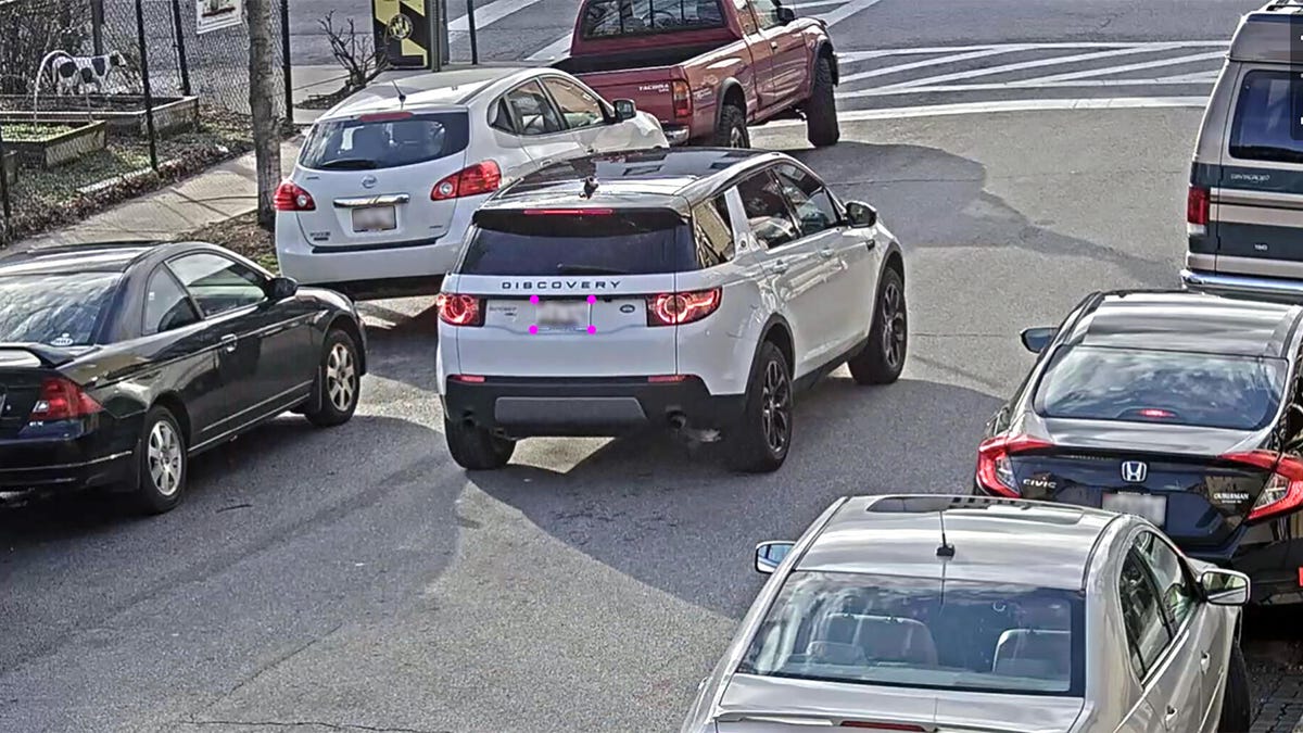 A car drives down a street with its license plate targeted by a camera.