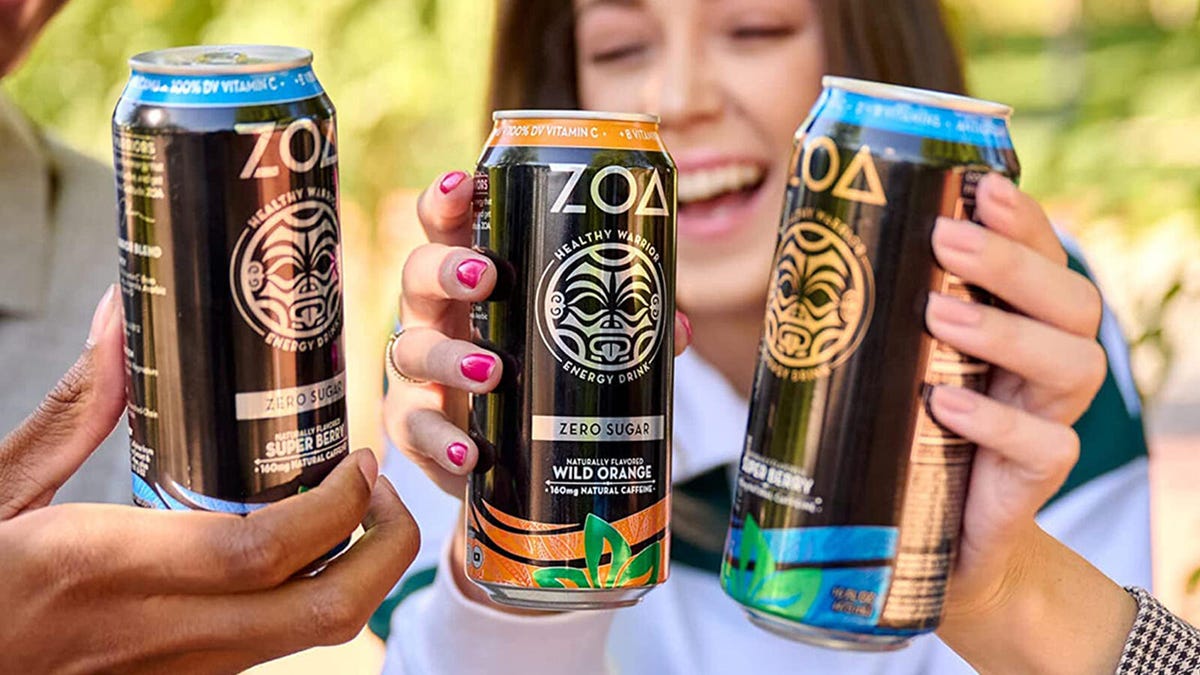 Three friends hold up cans of ZOA energy drinks while enjoying the outdoors.