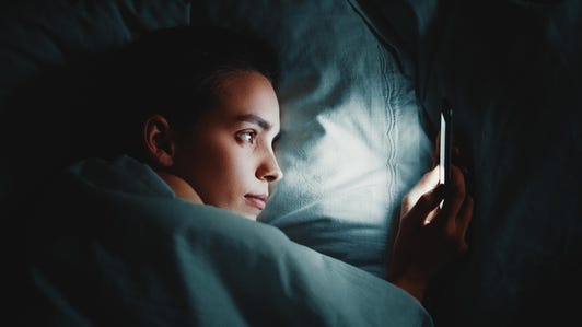 Close-Up Of Woman Using Phone While Lying On Bed In Darkroom