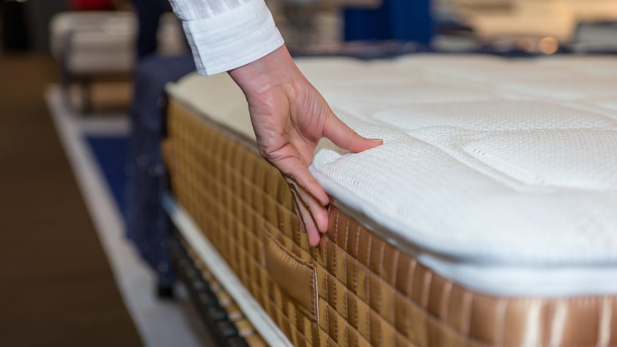 a hand presses a mattress in a showroom to test its firmness
