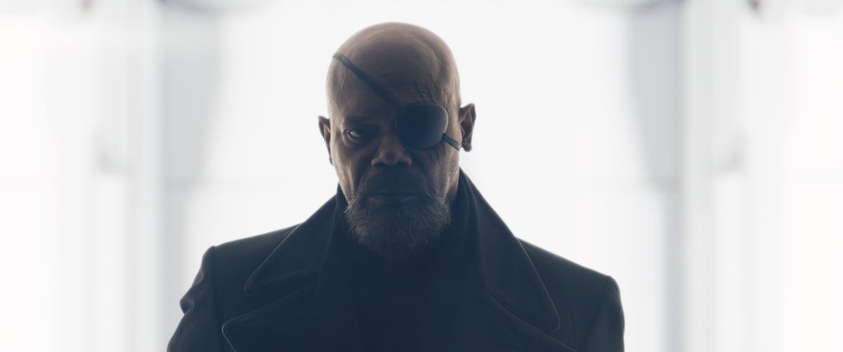 man dressed in a black trench coat wearing an eye patch looks to the side