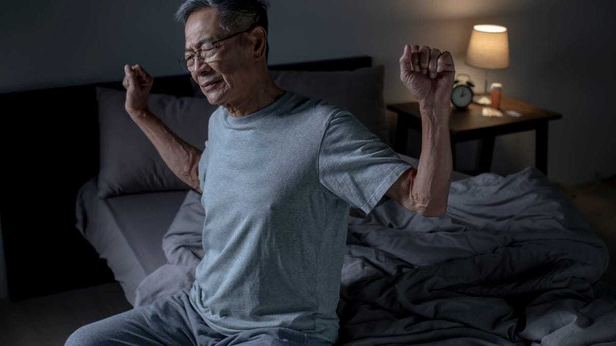 Older man stretching his arms out while struggling with back pain while sleeping.