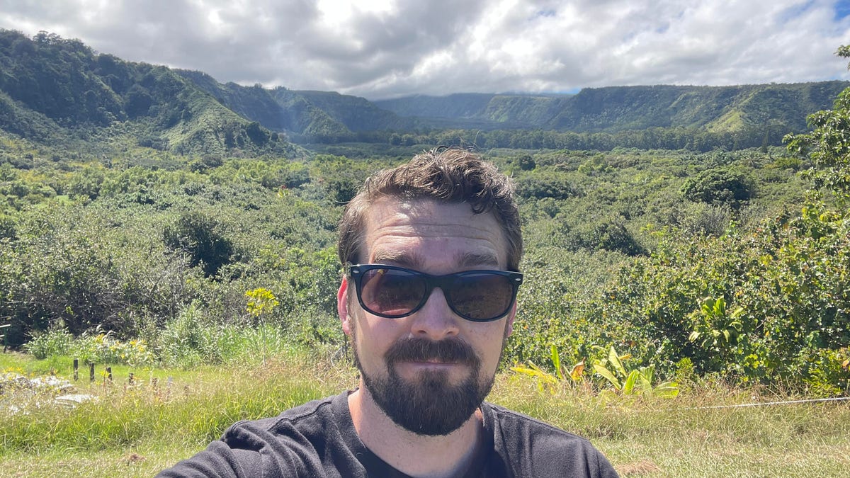 A man in sunglasses stands in front of Maui grassland.