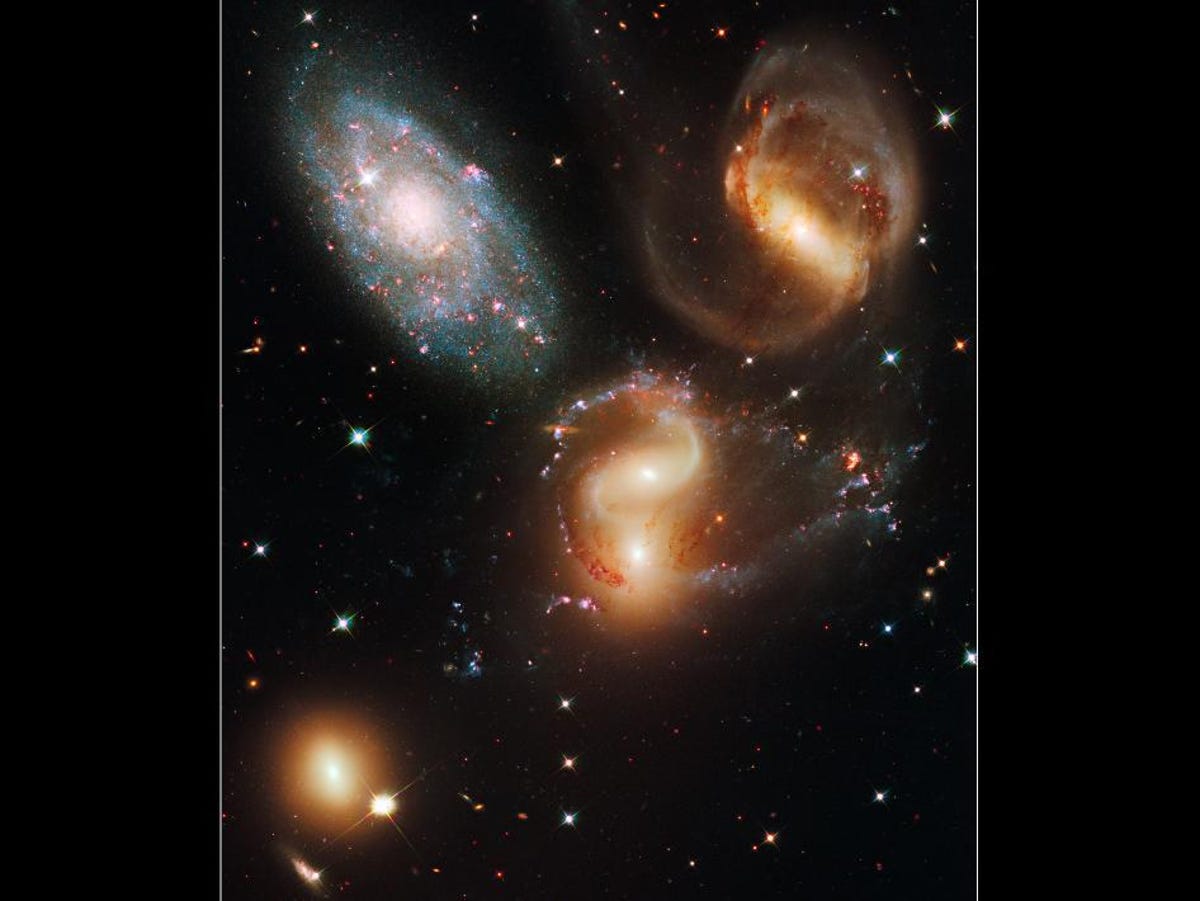 Hubble view of five galaxies looking like swirling objects of light against a color-flecked backdrop of space.