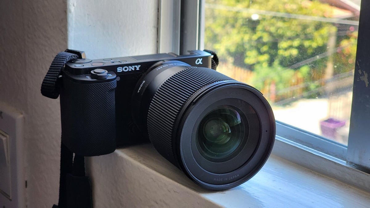 The Sony ZVE-10 mirrorless camera with a large Sigma lens, sitting on a window ledge.