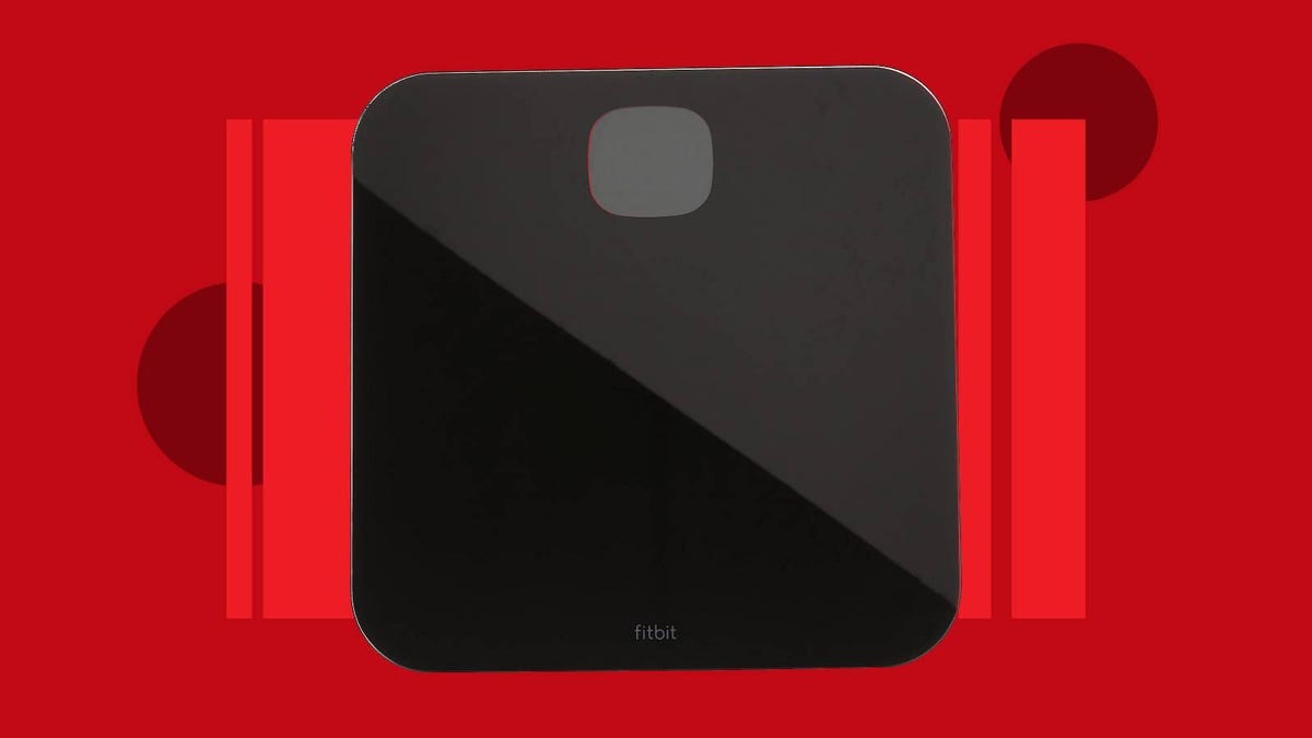 A black Fitbit smart scale against a red background.
