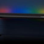 A dark image with a large black table and glowing rainbow lights