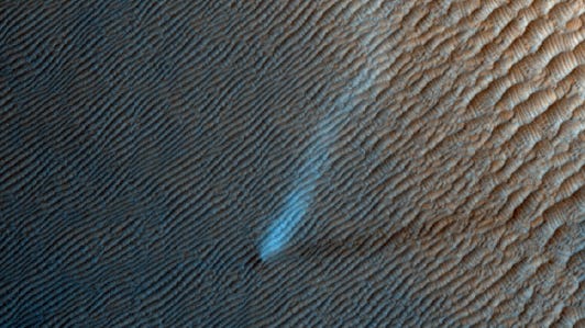 A color-processed image shows a long dust devil twisting across Mars dunes.