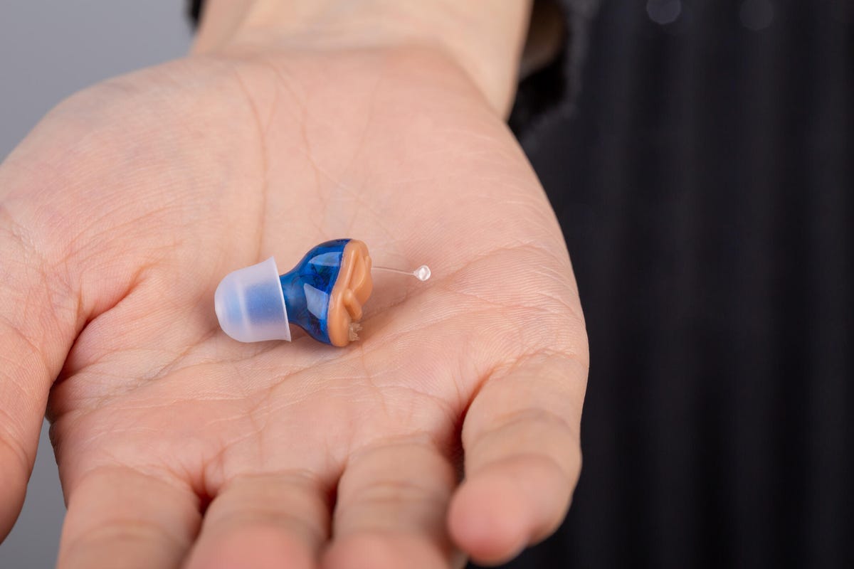 Person's hand holding a blue and orange hearing aid