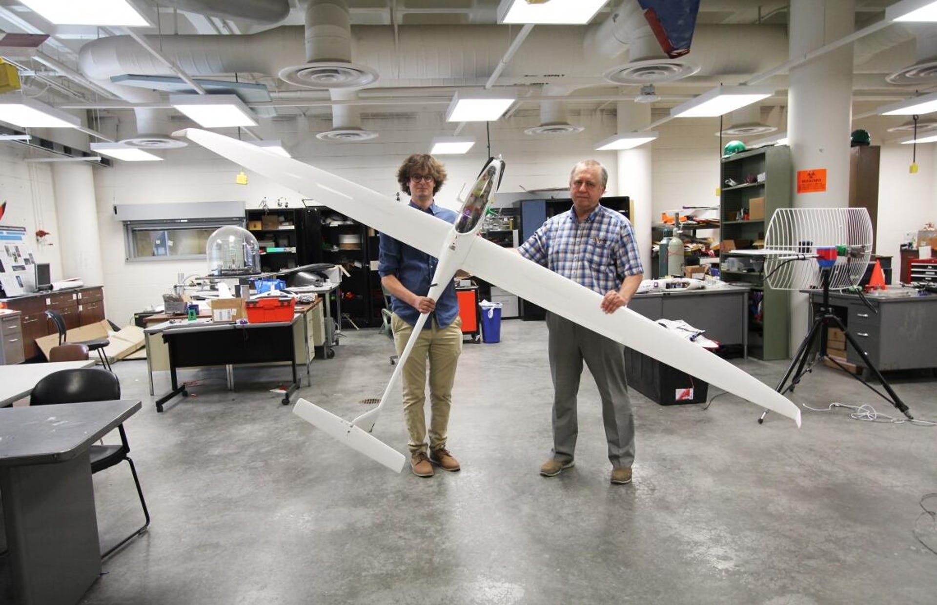 Two people stand in a room holding a white sailplane by the wings.