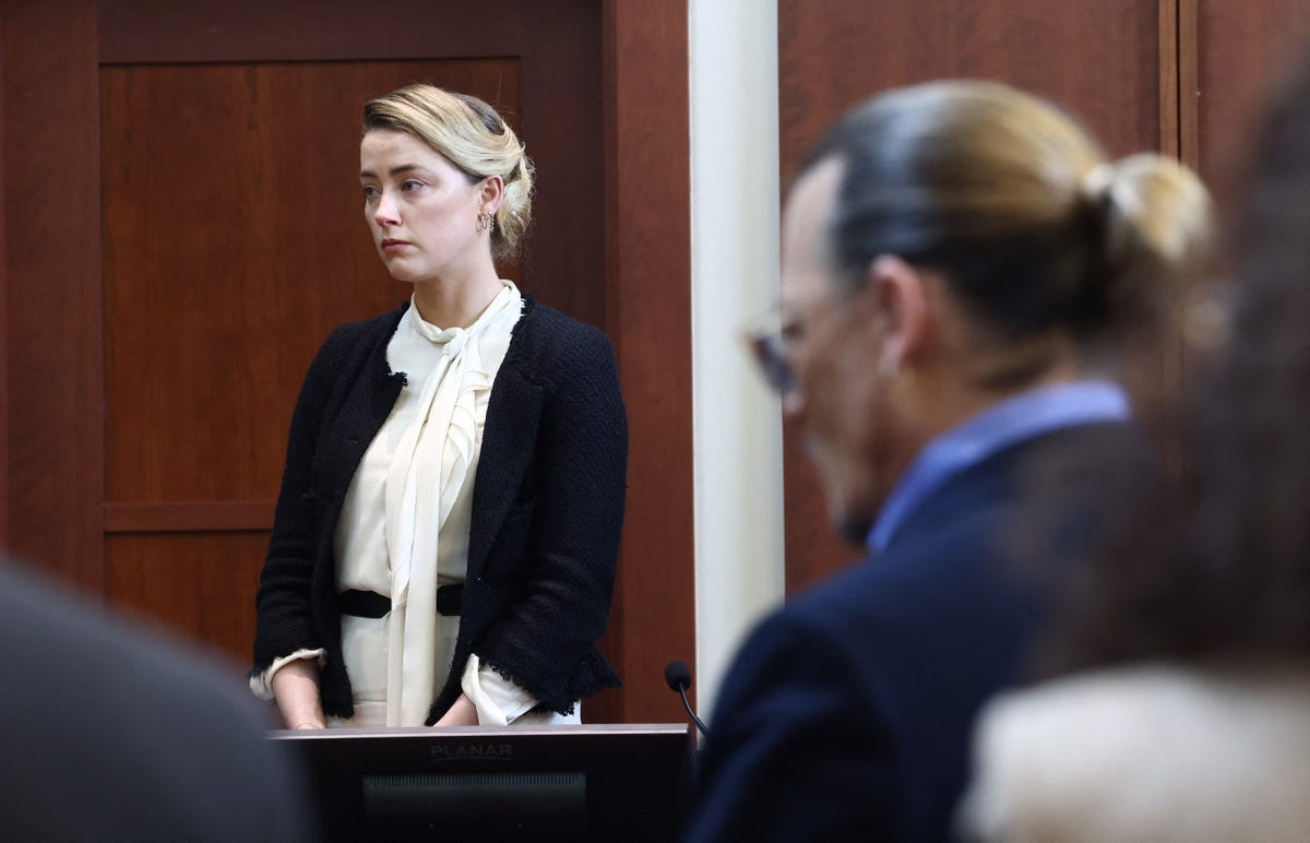 Amber Heard in the background of a courtroom, Johnny Depp in foreground.