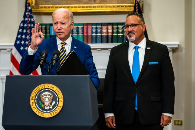 President Joe Biden and Secretary of Education Miguel Cardona stand at a podium
