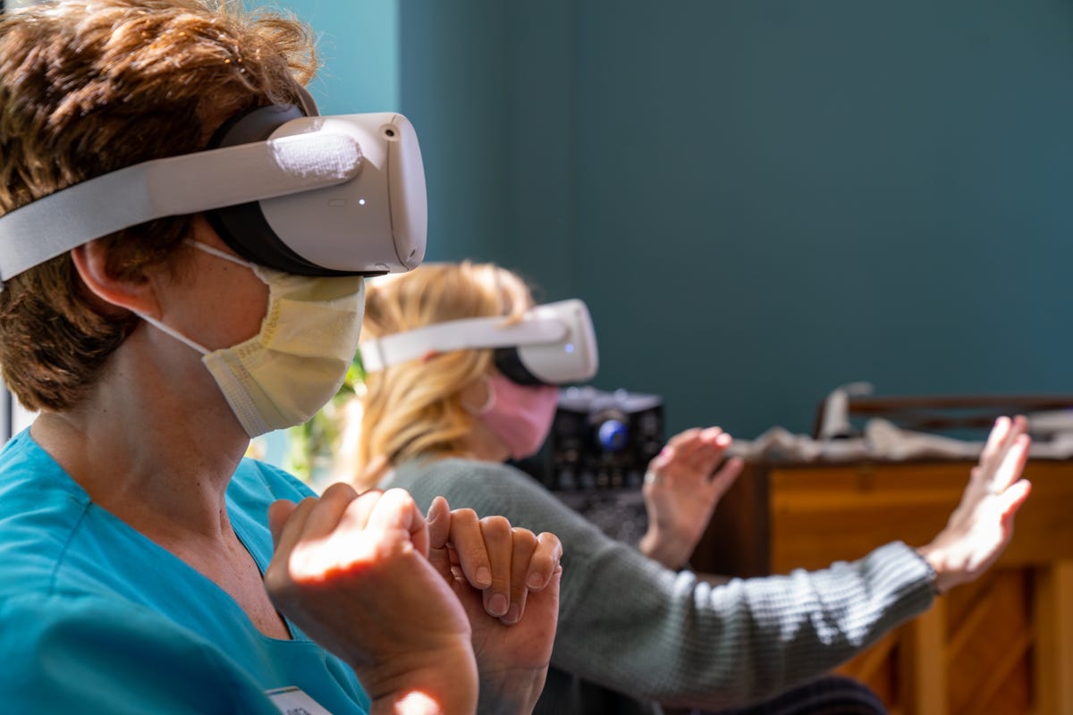 Two older women wearing VR headsets playing a game with their hands