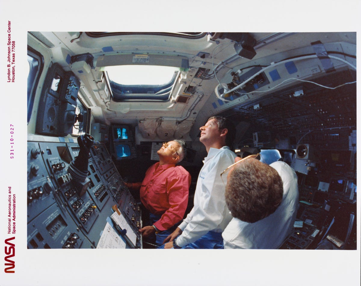 Three NASA crew members look out the window of Space Shuttle Discovery, observing Hubble in space.
