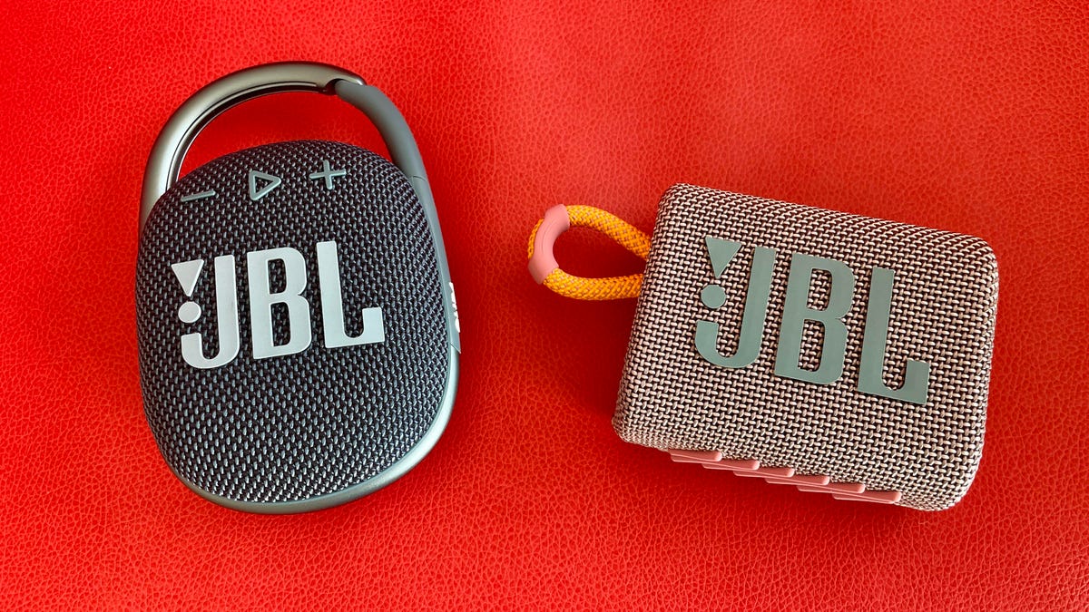 Two mini JBL Bluetooth speakers against a red background.