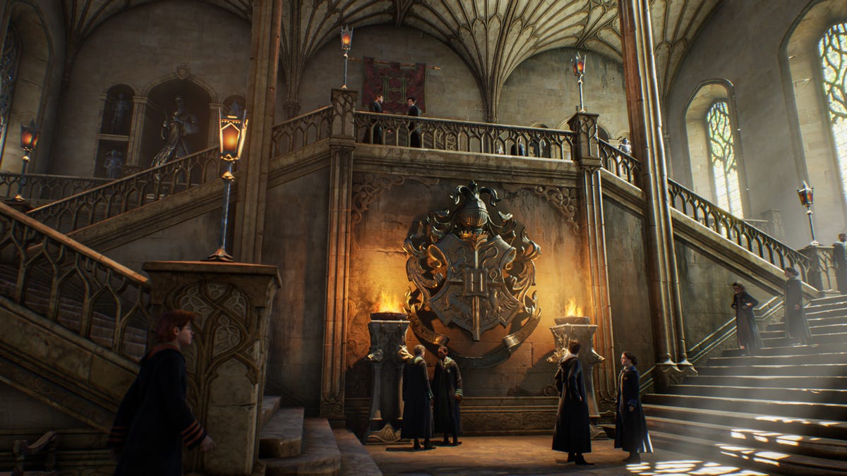 Students gather at the foot of the stairs in the stone entrance hall of Hogwarts in Hogwarts Legacy
