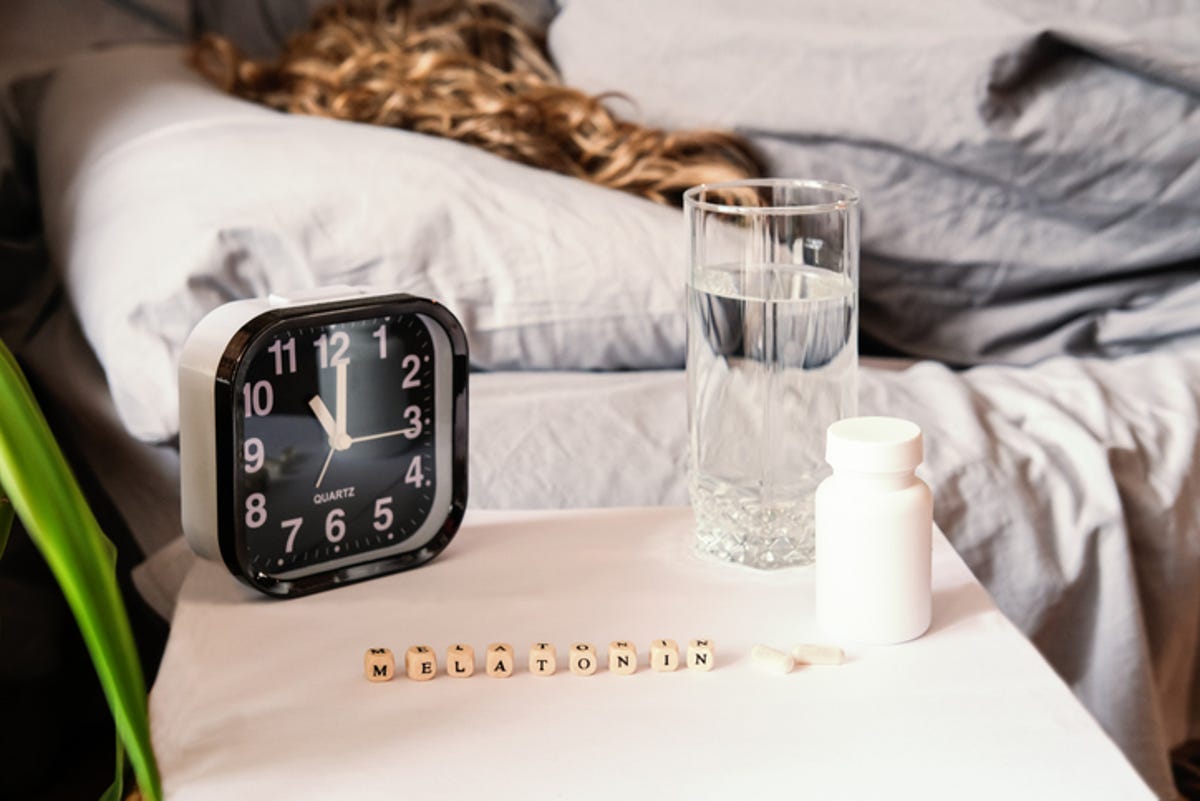 A melatonin supplement on the bedside table with an alarm clock and a glass of water.