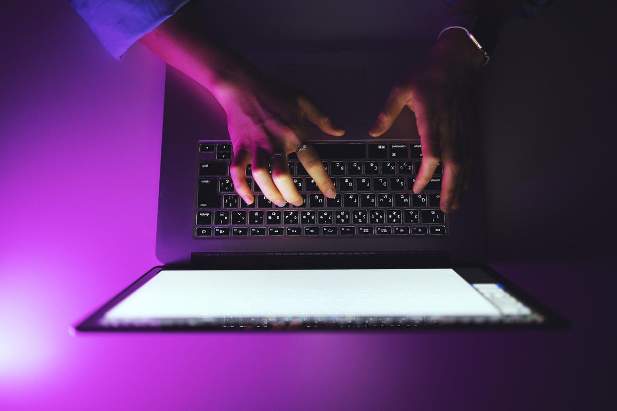 A person's hands typing with a purple backddrop