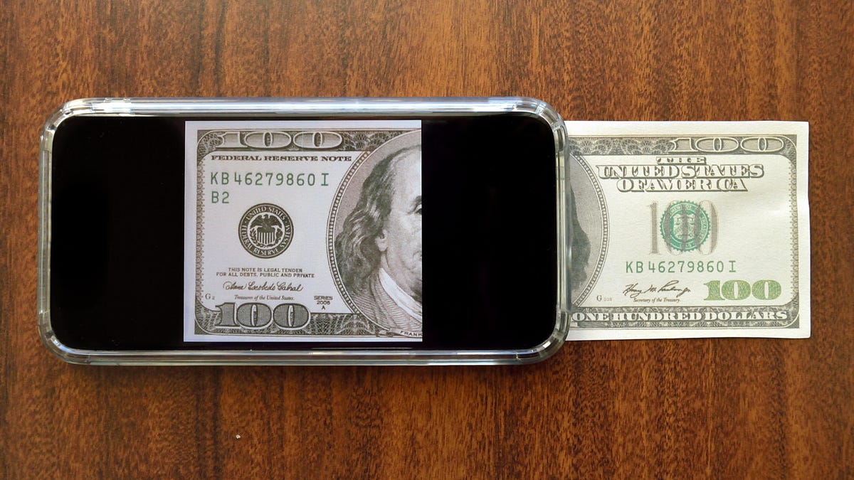 A phone on a table with a $100 bill shown emerging from the screen