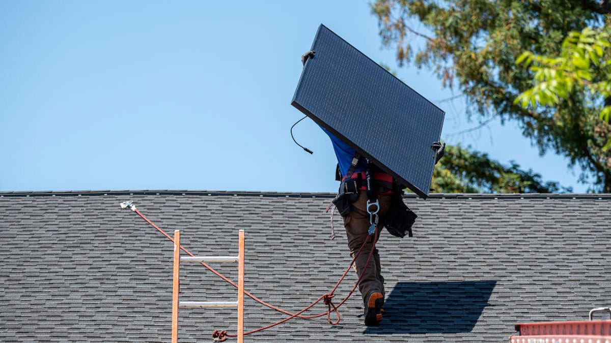 A worker installs a solar panel on a roof.