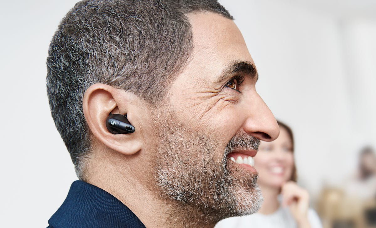 The Sennheiser Conversation Clear Plus earbuds in the ears of a man who needs a shave
