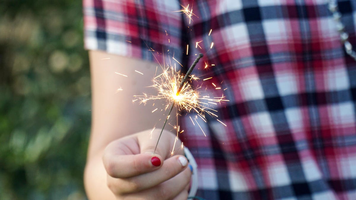 A person wearing red, white and blue holds a sparkler as it burns.
