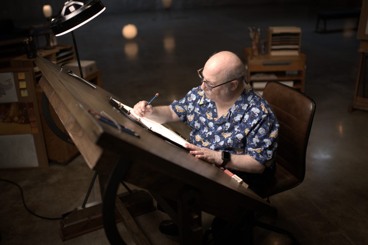 Disney animator Eric Goldberg sits at a drafting table in a large warehouse drawing the Genie from Aladdin.