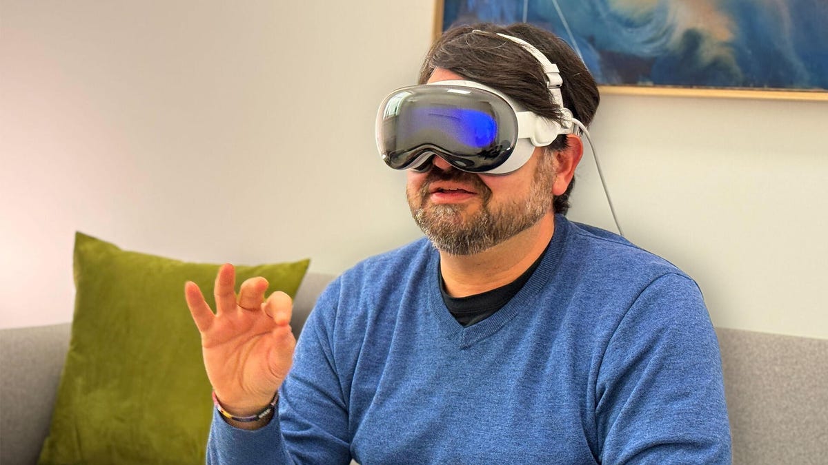 A man wearing the Apple Vision Pro VR/AR headset on, gesturing with his fingers