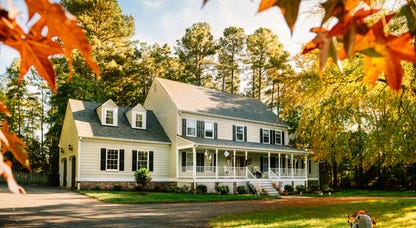 A two-story yellow house with a front porch surrounded by trees.