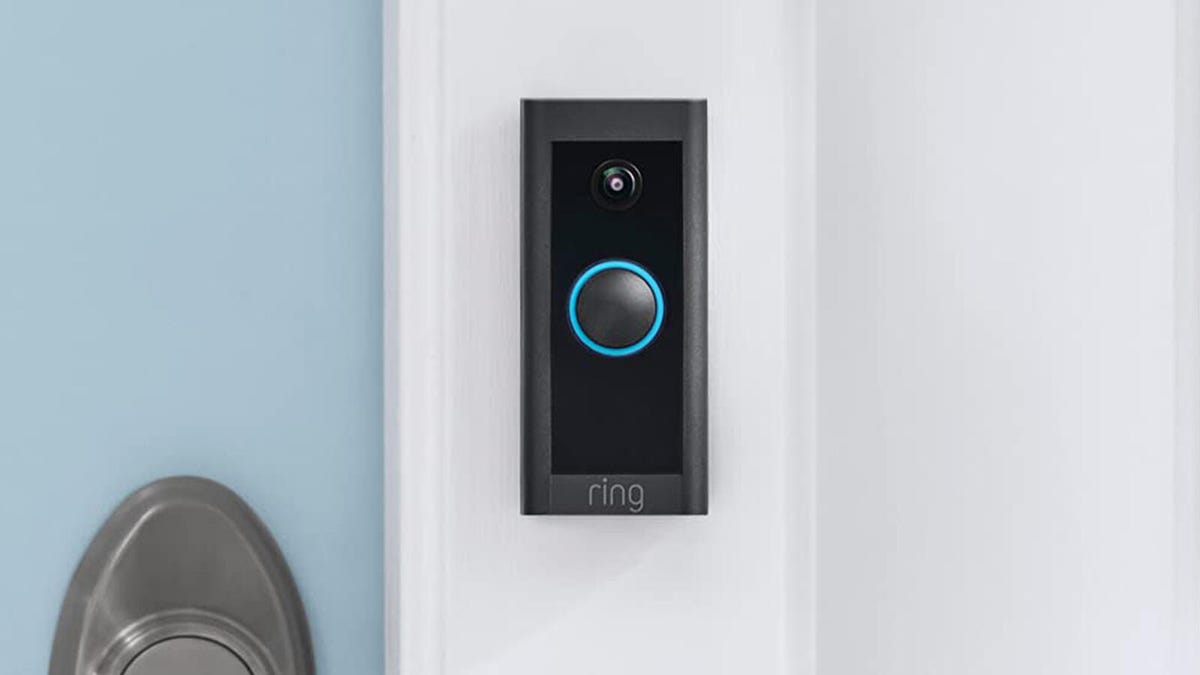 A black and gray Ring Video Doorbell Wired from 2021 is installed on a white doorframe besides a light blue door.