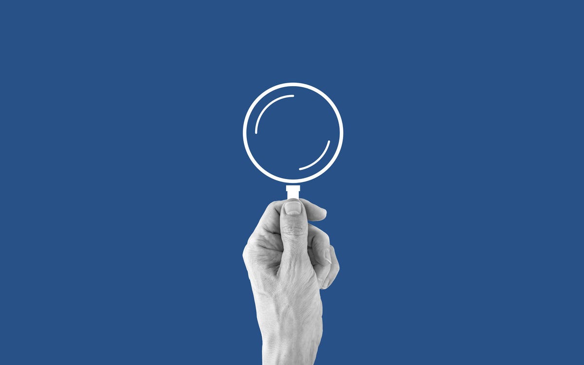 A hand holding a magnifying glass against a dark blue background