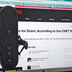 A grey microphone on a boom with Cnet open behind it