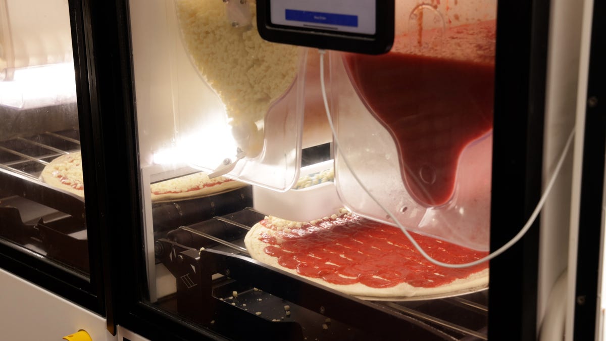 a machine adds toppings to a pizza base