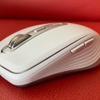 A White Logitech MX Anywhere 3 wireless mouse on a red chair.