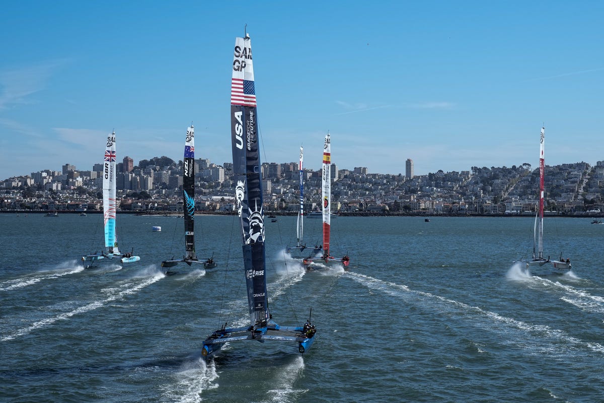 Six F50 sailboats race across the San Francisco Bay with the city skyline in the background.
