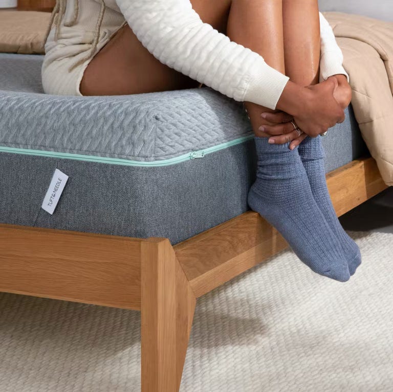Mujer con pantalones cortos y calcetines sentada en el borde de un colchón Mint, abrazando sus rodillas