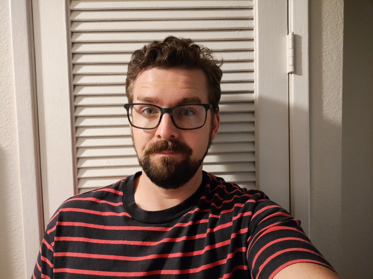 A man in a red and blue striped shirt looks into the camera.